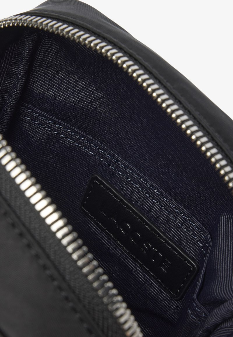 Intérieur d'un sac en tissu noir à texture lisse, avec une fermeture éclair argentée, doublé de tissu bleu foncé et une étiquette en cuir de marque.