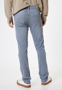 Vaqueros azul claro de corte recto, con dos bolsillos traseros y una tela texturizada. Llevados con zapatillas blancas y un suéter beige.