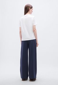 Λευκό βαμβακερό t-shirt με κοντά μανίκια, συνδυασμένο με φαρδιά σκούρα μπλε παντελόνια. Το παντελόνι έχει λεία υφή και διακριτικές πλαϊνές τσέπες.