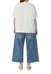 Witte katoenen t-shirt met een ontspannen pasvorm, gecombineerd met losse lichtblauwe denim culottes. Sandalen met kruislings gespen worden gedragen.