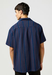 Korte mouw shirt in blauw met rode verticale strepen, geweven stof, button-down kraag en zijdelingse ventilatieopeningen. Beschikbaar in een ontspannen pasvorm.