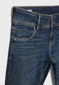 Jean en denim bleu foncé avec poches avant, passants pour ceinture et fermeture par bouton, présenté de la taille jusqu'à mi-cuisse sur un fond uni.