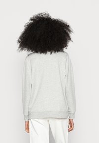 Sudadera gris de manga larga, con puños y dobladillo de canalé. Diseño sencillo con una textura suave; sin gráficos ni patrones visibles.