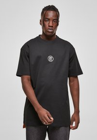 Juodas per didelis medvilninis marškinėliai su trumpomis rankovėmis, su apvaliu baltu logotipu priekyje ir tiesiomis siūlėmis.