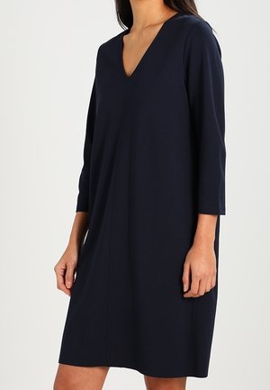 Robe bleu marine en tissu doux, avec un col en V, des manches trois-quarts et une coupe droite avec une couture centrale.
