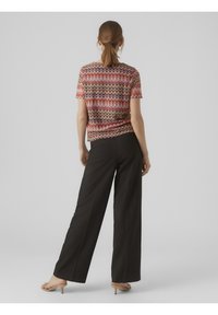 Kortærmet top med et zigzag mønster i pink, rød og sort, kombineret med højtaljede sorte brede bukser og beige sandaler.
