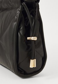 Black leather handbag with quilted texture, rounded shape, and gold hardware accents. Features zip closure with branded zipper pulls.
