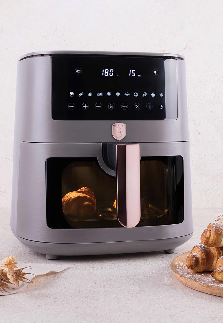 Friteuse à air moderne avec affichage numérique réglée à 180°C pendant 15 minutes, avec des croissants à cuire visibles à l'intérieur et sur une assiette en bois à proximité.