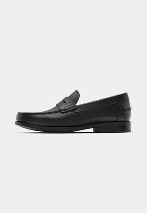 Mocassins en cuir noir avec un bout arrondi, des coutures détaillées et un petit talon carré. Texture lisse et design minimaliste.
