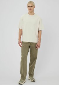 T-shirt oversize en crème en coton, associé à un pantalon droit olive et des baskets multicolores. Design épuré, détails minimaux.