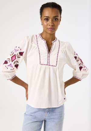 Witte blouse met roze en bordeauxrode geborduurde geometrische patronen op de mouwen, ronde halslijn en geraffineerd detail bij de buste. Duurzaam materiaal.