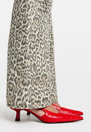 Photo prise à la longueur de la jambe d'un pantalon large imprimé léopard porté avec des chaussures à talon kitten pointues rouge vif avec une texture croco.