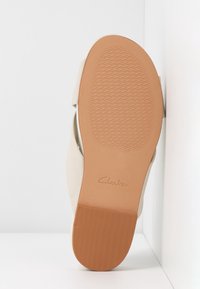 Semelle de chaussure beige avec un dessous en caoutchouc marron texturé, arborant un logo de la marque visible, des bords incurvés et un bord supérieur lisse.