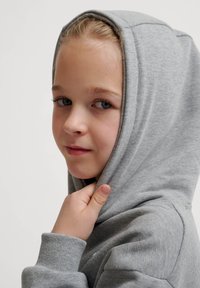 Szara bluza z kapturem, o miękkiej teksturze i prążkowanych mankietach. Model trzyma kaptur, prezentując prosty design.