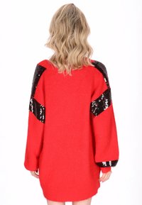 Rode oversized trui met lange mouwen, voorzien van zwarte paillettenaccenten op de schouders en een zachte, gestructureerde breisel afwerking.