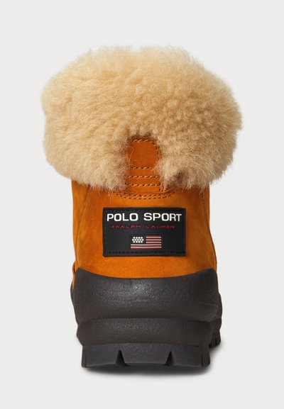 Πορτοκαλί σουέτ μποτάκι με καφέ τεχνητό γούνα στο κολάρο, μαύρη λαστιχένια σόλα και μαύρη ετικέτα που αναφέρει "POLO SPORT" και την αμερικανική σημαία.