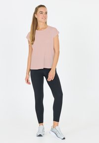 Vaaleanpunainen lyhythihainen paita, jossa on hienovaraisia raidoituksia, mustat legginsit ja harmaat urheilukengät, seisoo valkoista taustaa vasten.