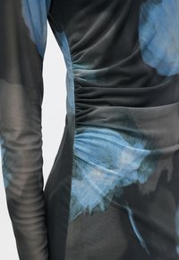 Černé a modré šaty se vzorem a žerzejovým designem, kombinující průsvitné a neprůhledné textury, zdůrazňující květinové motivy.