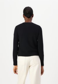 Zwarte gebreide trui met lange mouwen en een geribde zoom, met een V-vormige achterkant van de halslijn, gecombineerd met lichtgekleurde broek.