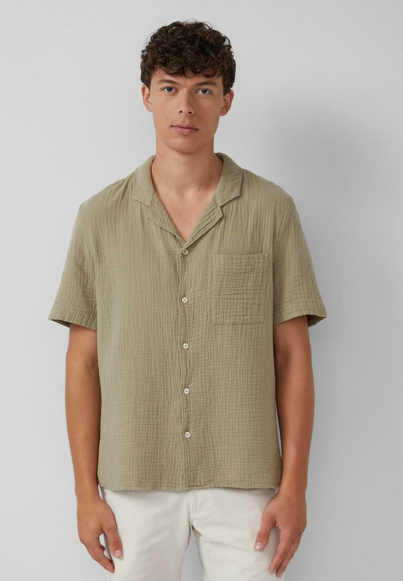 Kurzärmliges Button-up-Hemd in Olivgrün, aus zerknittertem Stoff, mit einer Brusttasche und einem lockeren Schnitt. Einfache weiße Knöpfe.