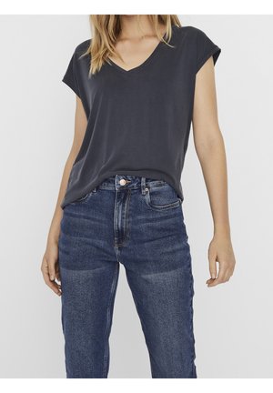 Woman wearing a dark gray V-neck short sleeve top tucked slightly into high-waisted blue jeans against a plain background.