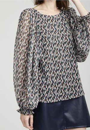 Woman wearing a long-sleeve, patterned blouse with puffed sleeves and ruffled cuffs paired with a dark mini skirt.