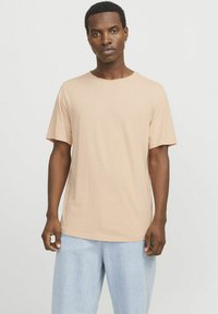 Light peach short-sleeve t-shirt made from soft fabric, featuring a crew neckline and relaxed fit, paired with light blue denim pants.