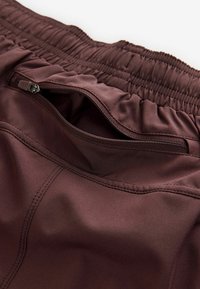 Bordeaux atletiske shorts med flad talje, elastik, en lynlåslomme og en glat, blank overflade.