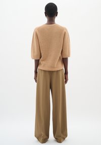 Hellbrauner Strickpullover mit kurzen Ärmeln, kombiniert mit hochtaillierten, weit geschnittenen braunen Hosen. Weiche Textur und lockere Passform.