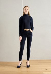 Navy cardigan over a black turtleneck, paired with dark skinny jeans and navy high-heeled shoes, accentuated by a beige belt.