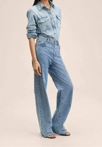 Chemise en denim bleu clair avec design à boutons, deux poches poitrine, associ ée à un jean taille haute à jambes larges bleu clair. Texture lisse.