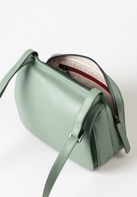Minzgrüne Ledertasche mit strukturiertem Design, Reißverschlussverschluss und einer Innentasche mit rotem Reißverschluss. Verstellbarer Schultergurt.