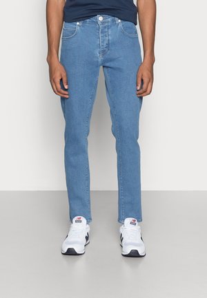 Hellblaue, gerade geschnittene Jeans aus Denim mit vorderen Taschen und einem Knopfverschluss. Kombiniert mit weißen Turnschuhen für einen lässigen Look.
