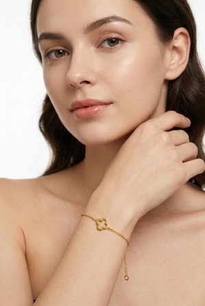 Nuori nainen, jolla on kirkas iho, käyttää herkkää kultaketjut rannekorua, jossa on nelilehtisen apilan riipus, valkoista taustaa vasten.