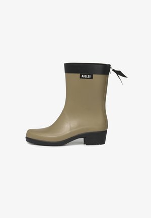 Botte de pluie en caoutchouc khaki avec un bandeau supérieur noir, bout rond et petit talon noir. Elle présente une tirette sur la fermeture éclair et un logo à l'avant.