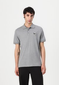 Siva polo majica iz mehkega materiala s klasičnim ovratnikom. Ima majhen grafični logotip na levem prsnem delu. Ravna krojna, kratke rokave.