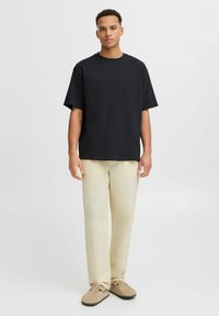 Sort kortærmet skjorte med rund hals, parret med beige bredbenede bukser. Sættet har en afslappet pasform og et minimalistisk design.