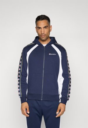Sudadera de cremallera navy con paneles laterales blancos, capucha con cordón y logotipos a lo largo de las mangas. Mezcla de algodón con puños y dobladillo de canalé.