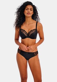 Conjunto de lencería negra que incluye un sujetador balconette con ribete de encaje floral y unas braguitas de estilo bikini a juego con lados de encaje transparente. Textura de tela suave.