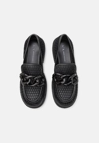 Černé lakýrky s texturovaným svrškem, zdobené robustním černým řetězem. Podešev je gumová s designem kulatého okraje.