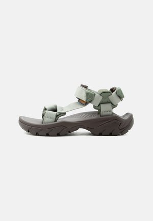 Outdoor sport sandal with adjustable light green straps and rugged dark gray sole, angled side view on a light gray background.