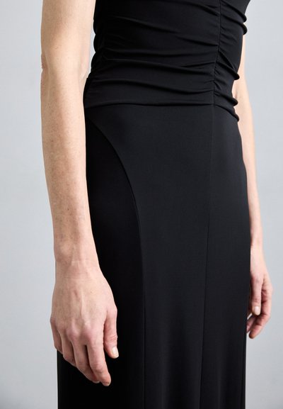 Vestido negro con cuerpo texturizado fruncido y falda suave. Presenta una silueta ajustada y un ligero drapeado en la cintura.