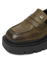 Hnedé kožené loafery s širokou čiernou gumovou podrážkou, majúce prešitý dizajn a kovový akcent na boku.