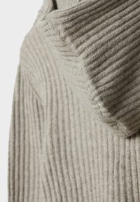 Pull en tricot beige clair avec une texture côtelée épaisse et un large col montant plié. Matière douce avec une coupe légèrement décontractée.