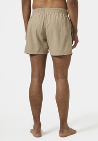 Bañador beige con cinturilla elástica, tejido ligero y corte por encima de la rodilla. Textura suave, diseño minimalista, sin patrones visibles.