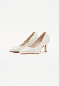 White high-heeled pumps with a pointed toe and faux leather texture. Features a sleek design with a low, sturdy heel and a nude interior.
