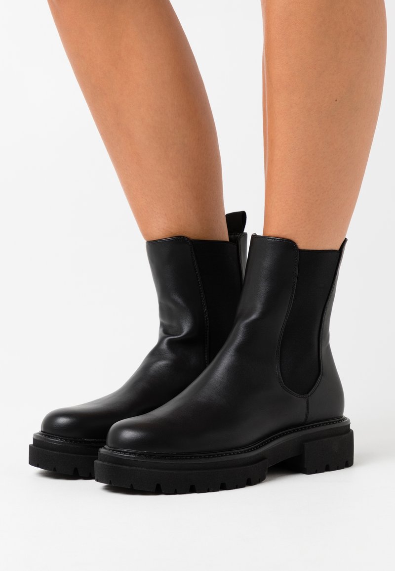 Botines negros de cuero con paneles laterales elásticos, puntera redondeada y suela texturizada y gruesa. Diseño minimalista con detalle de costura en contraste.