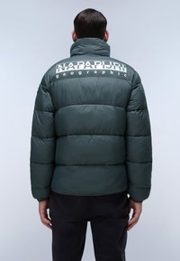 Giacca a vento verde con colletto alto, caratterizzata da un grande logo bianco sul retro. Texture liscia e design trapuntato con silhouette aderente.