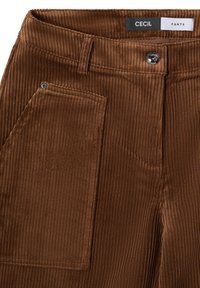 Bruine corduroy broek met verticale ribbels, voorzien van een knoopsluiting, riemlussen en een zijzak. Het label vermeldt "CECIL PANTS."