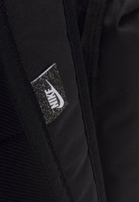 Zaino nero con un tessuto texturizzato, caratterizzato da un grande patch bianco con il logo Nike cucito di lato. Design semplice con spallacci imbottiti.